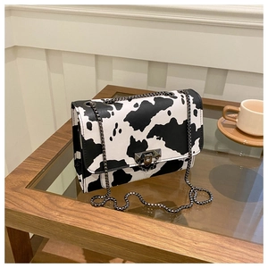 Detail of cow print crossbody bag with black and white pattern and grey chain strap