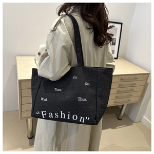 Detail of minimalist black canvas tote bag showing fashion text print and day abbreviations