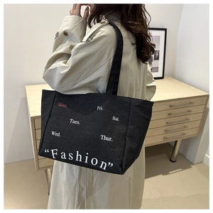 Detail of black canvas tote bag with Monday fashion print worn by a model in a warm room