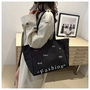 Detail of a black canvas tote bag with fashion lettering worn by a model in a beige coat