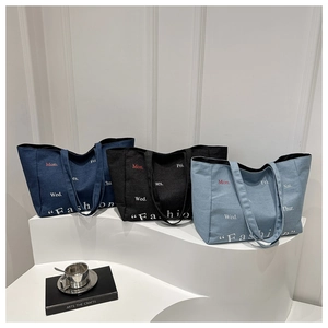 Three minimalist large denim tote bags in black and blue shown on a display stand