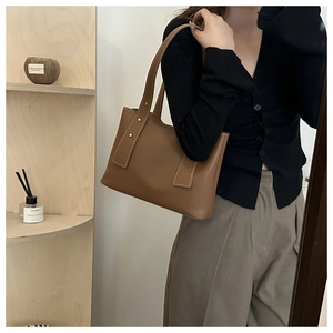 Detail der karamellbraunen Bucket Bag aus Leder mit Goldnieten und vertikalen Riemen