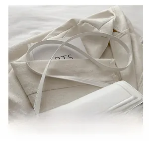 Détail d'un petit sac carré blanc minimaliste en cuir mat avec boucles métalliques dorées