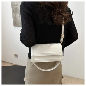 Détail du sac bandoulière blanc brillant avec boucle dorée et surpiqûres texturées