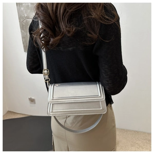 Détail d'un sac bandoulière argenté métallisé avec surpiqûres et boucle dorée élégante