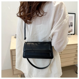 Détail d'un sac à bandoulière rectangulaire en cuir noir mat porté par un modèle
