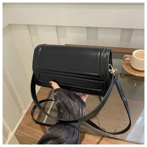 Détail d'un sac bandoulière noir en cuir avec coutures rectangulaires et boucles dorées