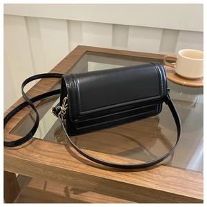 Détail du sac à bandoulière noir en similicuir avec boucles dorées sur une table