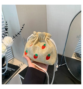 Close-up of beige woven bucket bag with detailed red strawberry embroidery and drawstrings