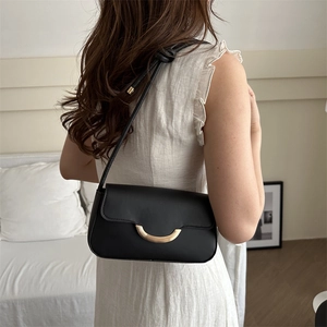 Minimalist black leather underarm bag with gold metal clasp shown on a model