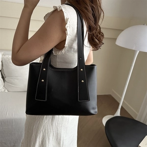 Black leather bucket bag with white contrast stitching and gold metal rivet accents