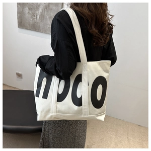 Détail d'un grand cabas en toile blanche avec logo hoco noir porté par un mannequin