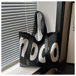 Detail of a large black tote bag with white lettering and reinforced leather straps