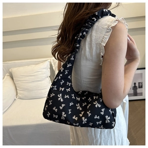 Detail of black tote bag featuring white bow patterns and pleated cloud shoulder strap