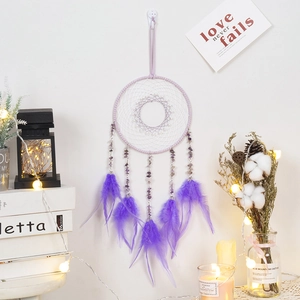 Purple dream catcher with amethyst stones and feathers hanging on a white wall