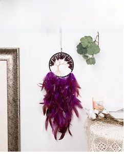 Detail of tree of life dreamcatcher with purple feathers and natural stones on a white wall