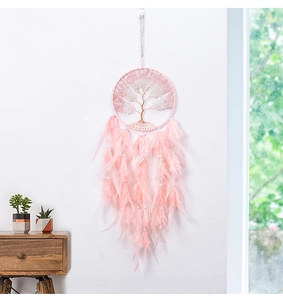 Pink Tree of Life dream catcher with feathers and stones hanging in a cozy room