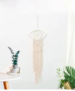 Close-up of bohemian hand-woven eye tapestry with long cotton tassels on white wall