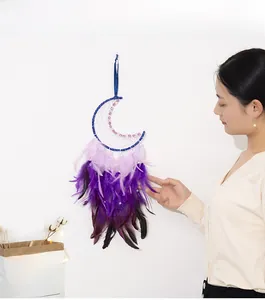 Détail d'un attrape-rêve en forme de lune avec plumes violettes tenu par une femme