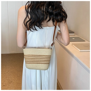 Detail of striped straw crossbody bag with brown leather strap worn over white dress