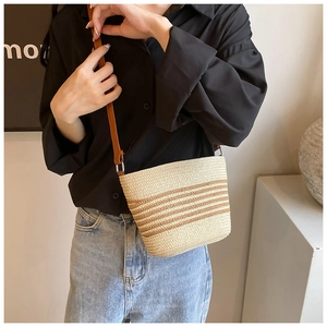 Detail of a straw crossbody bucket bag with brown stripes and a leather shoulder strap