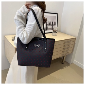 Woman wearing a black tote bag with red heart pattern and silver bow decoration