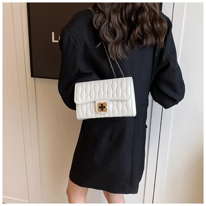Detailed view of white quilted crossbody bag with gold flower buckle on black suit