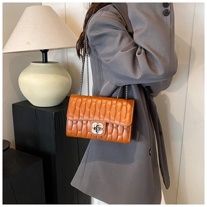 Detail of orange-brown quilted crossbody bag with floral metal lock and silver chain