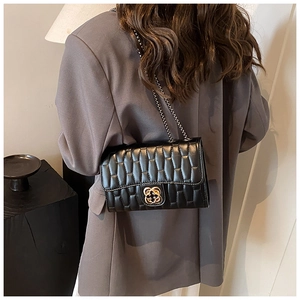 Model wearing a black quilted crossbody bag with golden flower clasp and chain strap
