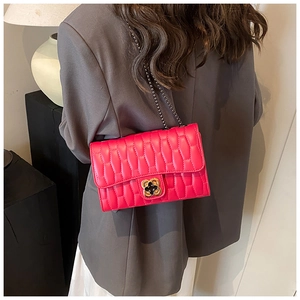 Detail of rose red quilted crossbody bag with gold flower clasp on grey blazer
