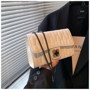 Detail of white quilted crossbody bag featuring a golden flower twist lock and chain