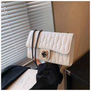 Close-up of white quilted crossbody bag featuring a gold flower twist lock and chain