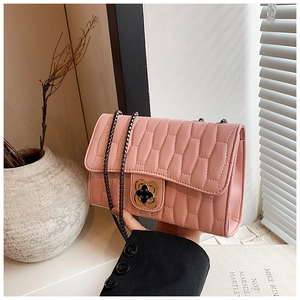 Pink quilted crossbody bag with gold clover clasp and chain strap held in hand