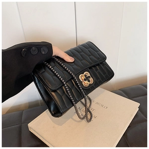 Detailed close-up of black quilted shoulder bag with golden floral metal buckle and chain strap