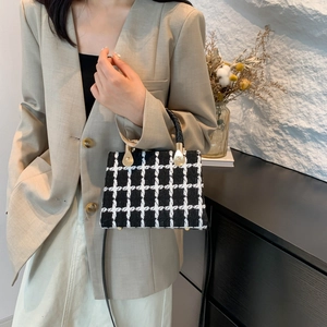 Chic black and white checkered tweed crossbody bag with gold hardware held by a model