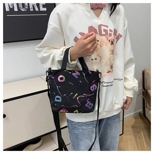 Détail du sac cabas noir avec lettres colorées porté avec un sweat blanc décontracté