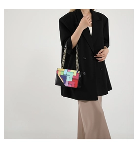 Detail of colorful geometric patchwork handbag with metal chain strap on model