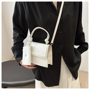 Minimalist white crossbody bag with detachable pouch shown in a styled fashion pose