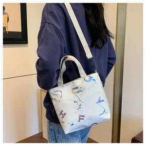 Détail du sac seau blanc en toile avec lettres laser irisées et bandoulière