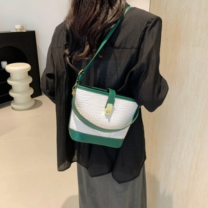 Chic white woven bucket bag with green leather trim shown on a model in a minimalist room