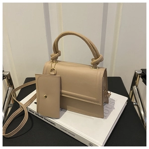 Detail view of beige crossbody bag with knotted handle and mini pouch on white books