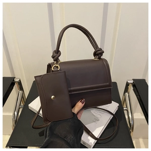 Detail of dark brown leather crossbody bag with knot handle and gold chain on magazine