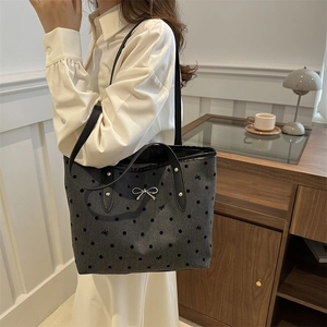Grey tote bag with bow embroidery and black leather straps in a lifestyle setting