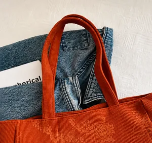 Close-up of rust red corduroy tote bag showing reinforced handles and ribbed texture