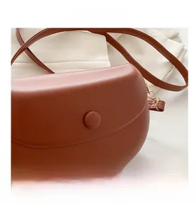 Detail view of brown leather saddle bag featuring a gold magnetic buckle and slim strap