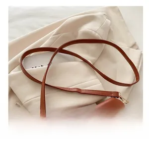 Close-up of a brown leather saddle bag with gold metal buckle on a cream blazer