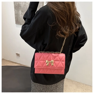 Detailed view of pink quilted crossbody bag with golden bow hardware on model back