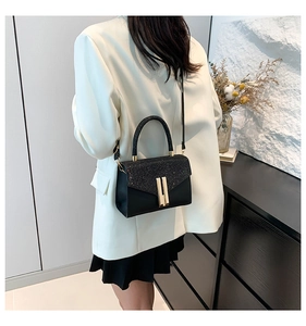 Detailed view of elegant black leather handbag with glitter flap and gold hardware on model