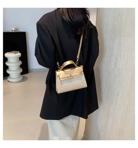 Detalle del bolso Kelly oro champán con cuero brillante y purpurina sobre un blazer negro