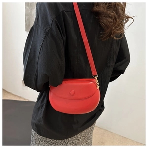 Red leather saddle bag worn by model featuring a minimalist semi-circle flip design